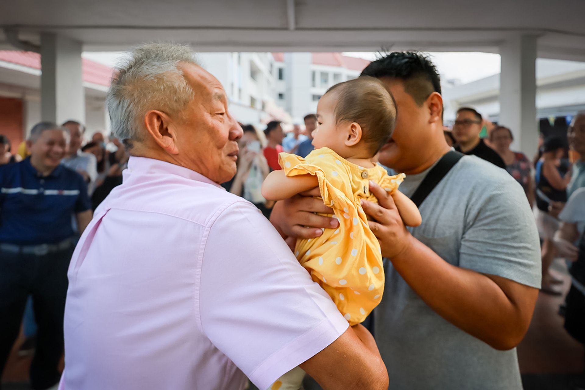 Mr Ng taking 13-month-old Sophie into his arms at the request of her father Darren Ong, 34, for a photo with his family during the presidential candidate’s visit to Tampines Round Market and Food Centre on Aug 27, 2023. ST PHOTO: GAVIN FOO